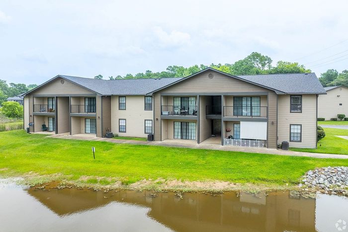 Charming two-story apartment complex with private balconies, nestled in a serene lakeside setting with lush green lawns.