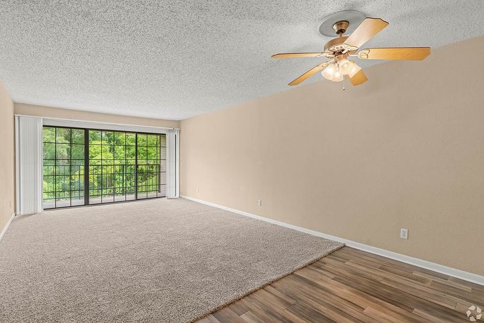 Bright living area with elegant ceiling fan and expansive window views of lush greenery, enhanced by plush carpeting and sleek wooden flooring.