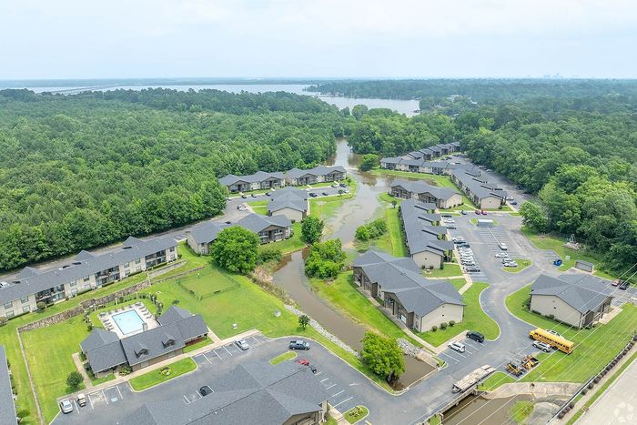 Scenic aerial view of a tranquil apartment community nestled in lush greenery with a serene pond and inviting swimming pool.