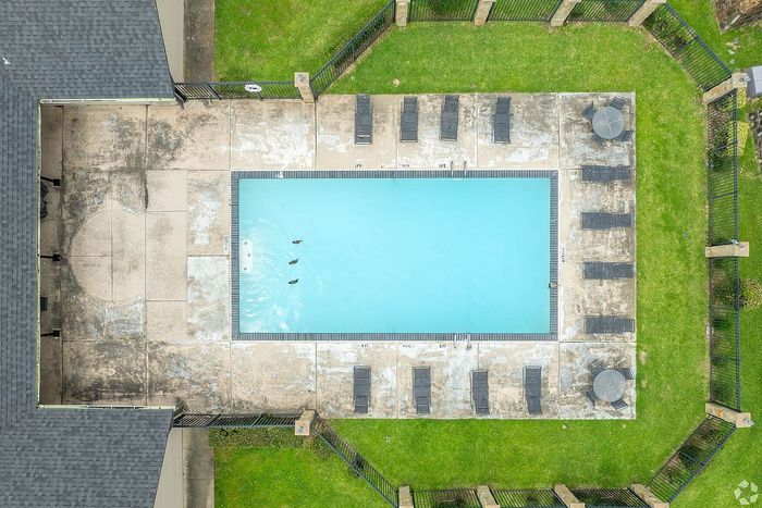 Aerial view of a sparkling swimming pool surrounded by lush green lawns and comfortable lounge chairs, offering a serene and inviting outdoor escape.
