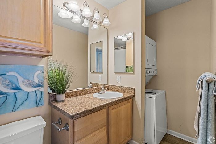 Cozy bathroom featuring a sleek granite countertop, elegant vanity lighting, and convenient in-unit laundry.