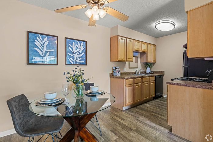 Charming dining area with a stylish glass table and two chairs, adjacent to a cozy kitchen featuring modern appliances and warm wooden cabinets.