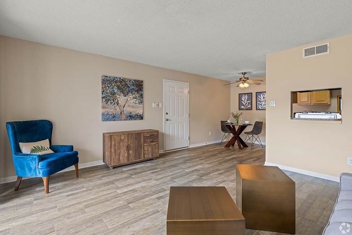 Charming living room with elegant blue armchair, modern wooden console, and stylish dining area, featuring warm neutral tones and artistic decor.
