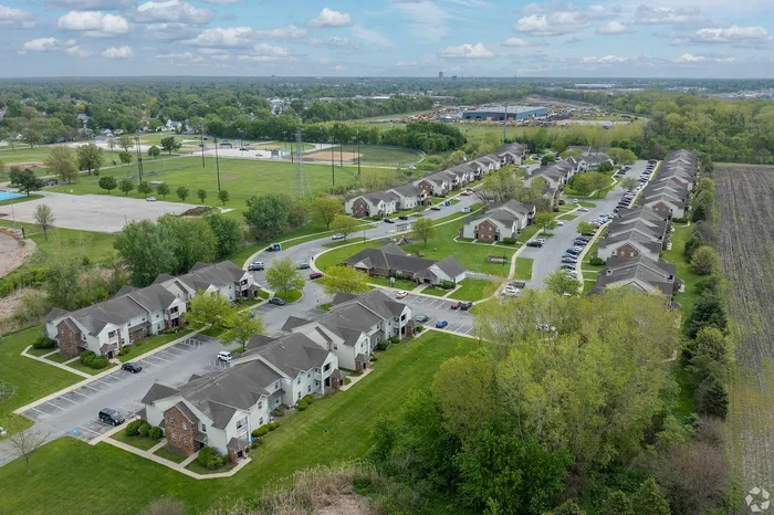 Scenic aerial view of a charming suburban apartment complex surrounded by lush greenery and expansive recreational fields.