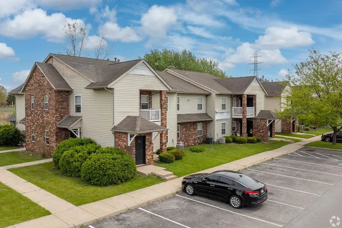 Charming apartment complex with beautiful brick and siding facade, set amidst lush greenery and clear blue skies, featuring convenient parking and inviting walkways.