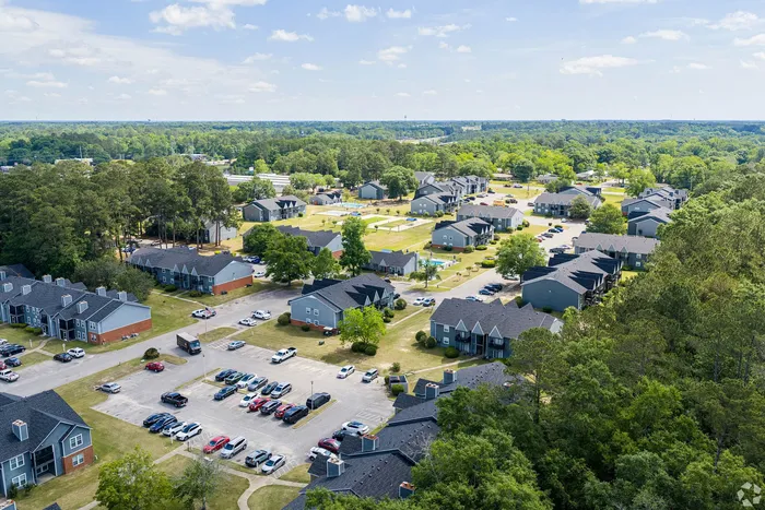 Scenic aerial view of a sprawling residential community surrounded by lush greenery, highlighting modern apartment buildings and spacious parking areas.