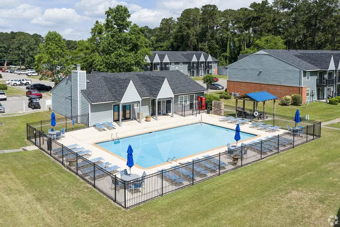 Inviting community pool area surrounded by lounge chairs and vibrant umbrellas, offering a relaxing escape amidst lush green landscaping.