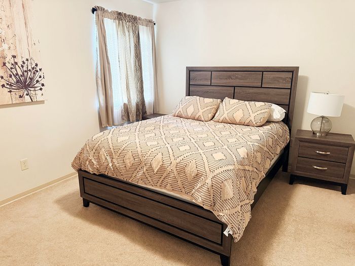 Cozy bedroom with modern wood furniture, soft beige carpet, and elegant decorative touches, offering a warm and inviting atmosphere.