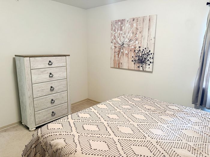 Chic bedroom with elegant dresser and modern art, featuring a cozy geometric bedspread and soft natural light.