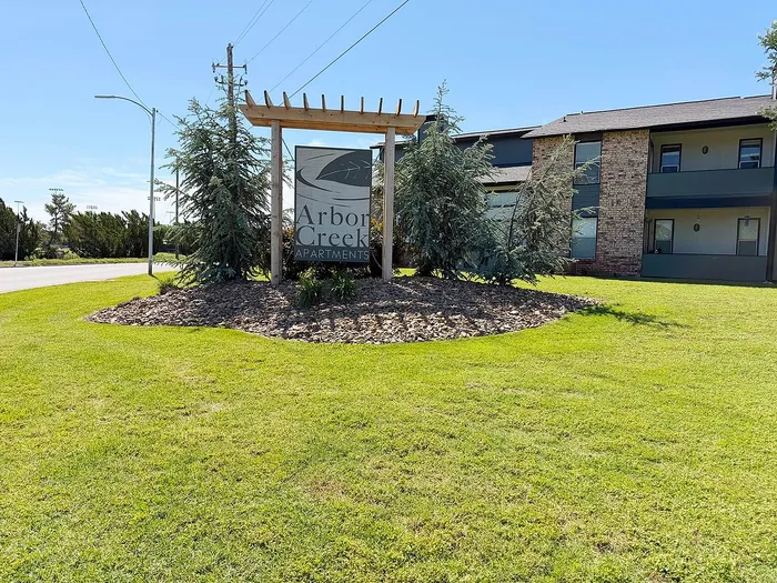 Inviting Arbor Creek Apartments entrance with lush greenery and modern brick exteriors.