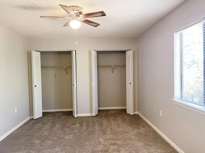 Bright, airy bedroom with dual closets, plush carpeting, and a large window for natural light.