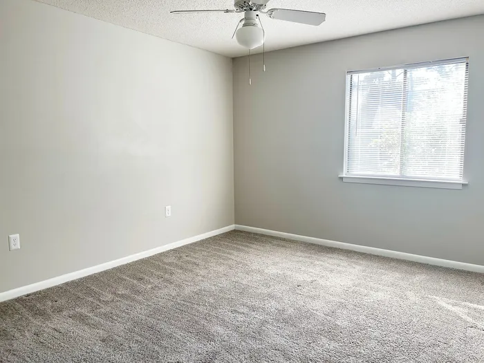 Bright and inviting empty room showcasing soft carpeting, neutral walls, and a large window letting in natural light, perfect for a cozy retreat.