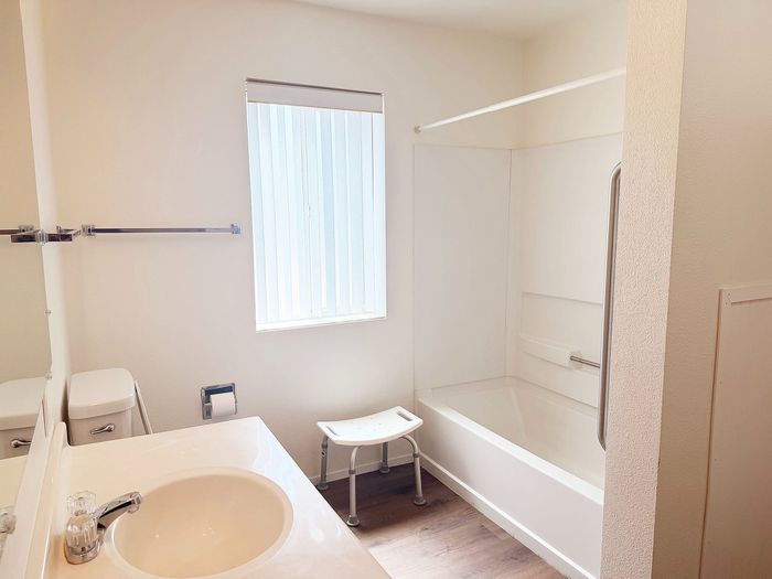 Bright and modern bathroom featuring a sleek white sink, bathtub, and natural light streaming through a large window.