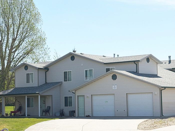 Charming duplex with modern design, featuring a cozy front porch and spacious garages, surrounded by lush greenery.