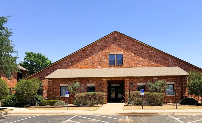 Charming red brick building with pristine landscaping and accessible parking, set against a clear blue sky.