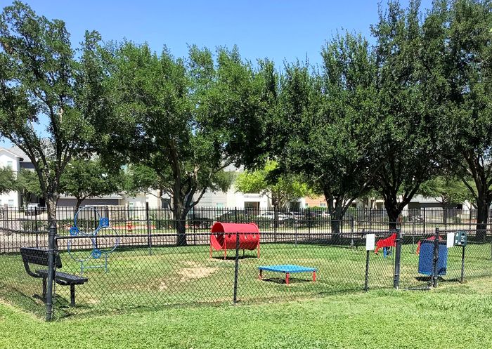 Charming outdoor dog park with agility equipment, surrounded by lush greenery and spacious seating areas.