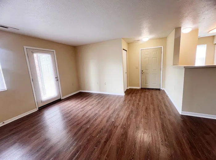 Inviting living room with elegant hardwood flooring and natural light, featuring modern entry and patio doors.