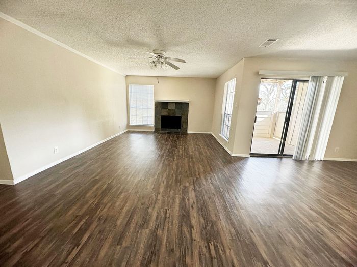 Spacious living room with elegant hardwood floors, a cozy fireplace, and sliding glass doors leading to a private balcony.