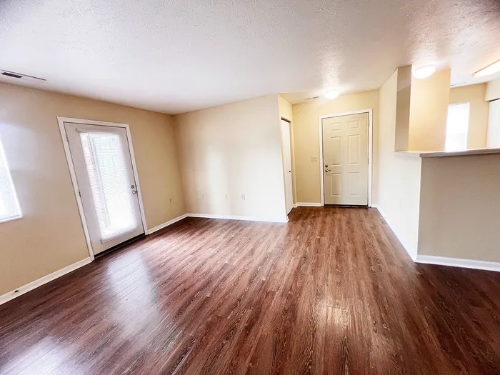 Bright and inviting open-plan living area with elegant wooden flooring and ample natural light from large windows.