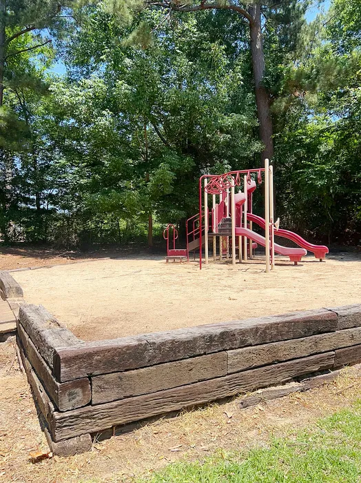 Inviting playground surrounded by lush green trees, featuring vibrant red slides and climbing structures on a sunny day.