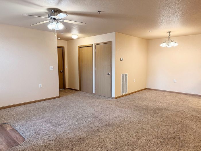 Bright living room with plush carpet, ceiling fan, and elegant lighting, offering spacious comfort and style.