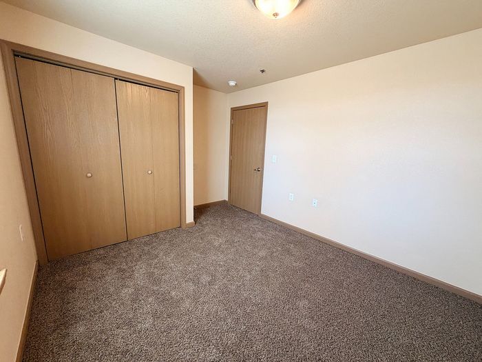 Bright, open room with plush carpet and wooden closet doors, perfect for creating a cozy bedroom retreat.