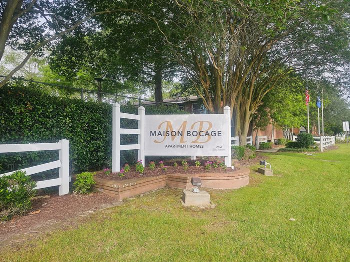 Inviting front entrance at Maison Bocage Apartment Homes showcasing a well-maintained garden and elegant signage surrounded by lush greenery.