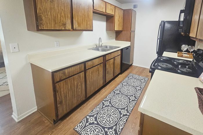 Charming kitchen with wood cabinetry, modern appliances, and sleek countertops, featuring a decorative runner on hardwood flooring.