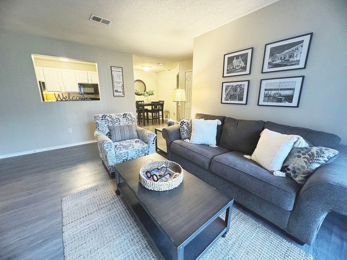Inviting living room with chic grey sofa, stylish armchair, and modern decor, seamlessly connecting to a cozy dining area and open-concept kitchen.