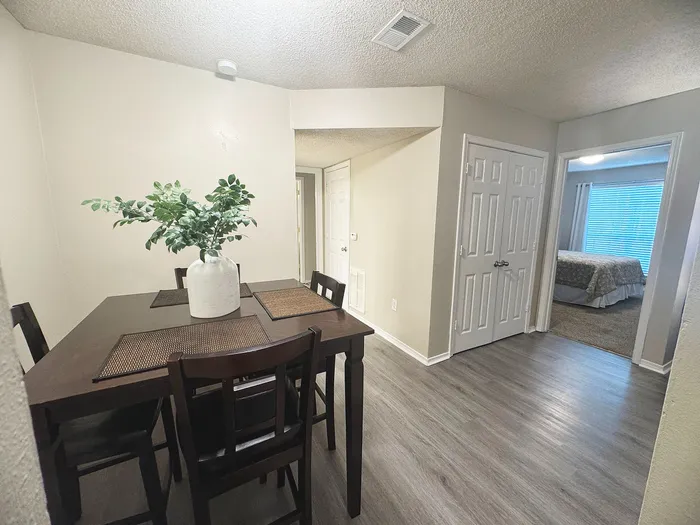 Inviting dining area with modern table set, leading to a cozy bedroom, featuring stylish flooring and soft lighting.