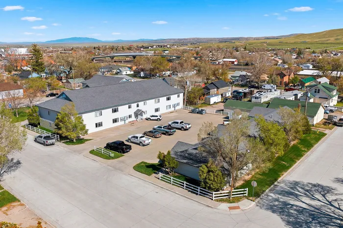 Charming aerial view of a spacious residential building with ample parking, nestled in a picturesque suburban neighborhood with scenic mountain backdrop.
