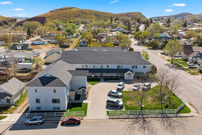 Charming apartment building with ample parking and a picturesque suburban setting surrounded by lush greenery and rolling hills.