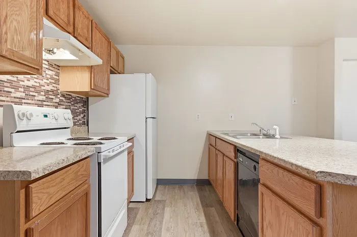 Modern kitchen featuring sleek wooden cabinets, a white refrigerator, stove, and dishwasher, accented by a stylish mosaic backsplash.