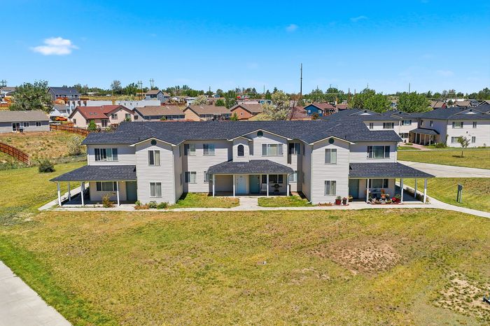 Charming two-story apartment complex with modern design, surrounded by lush greenery in a peaceful neighborhood setting.