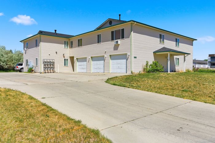 Charming multi-unit building with attached garages, surrounded by lush greenery and a spacious driveway.