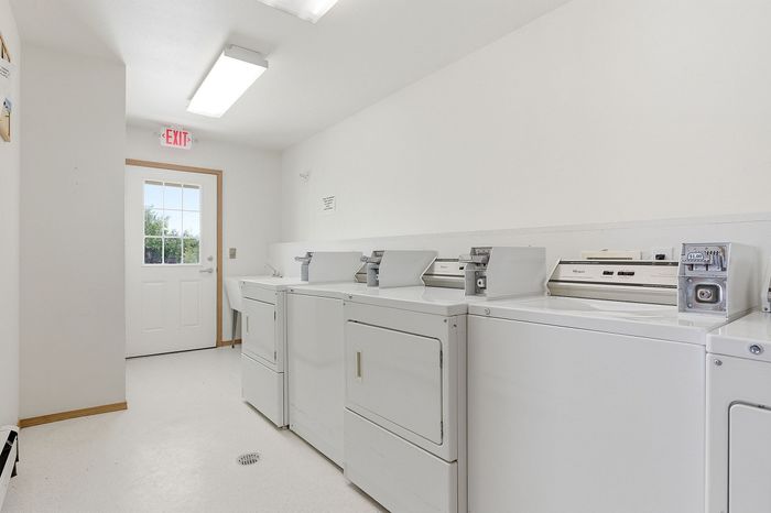 Bright and airy laundry room featuring modern coin-operated machines, pristine white walls, and ample natural light through a glass door.