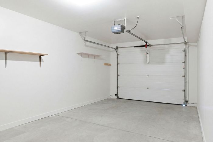 Spacious modern garage with pristine white walls, sleek overhead shelving, and a durable door, ideal for versatile storage and parking solutions.