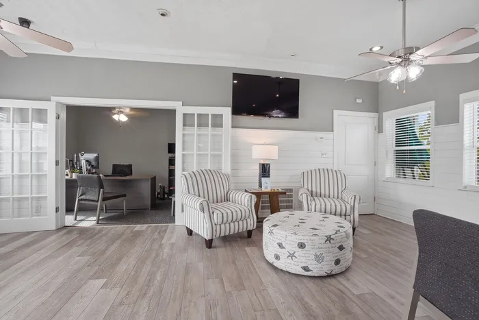 Inviting living room with elegant striped armchairs, stylish ottoman, and natural light streaming through large windows, ideal for relaxation and comfort.