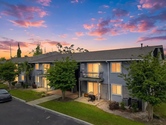 Charming two-story apartment building with cozy balconies and lush landscaping during a vibrant sunset.