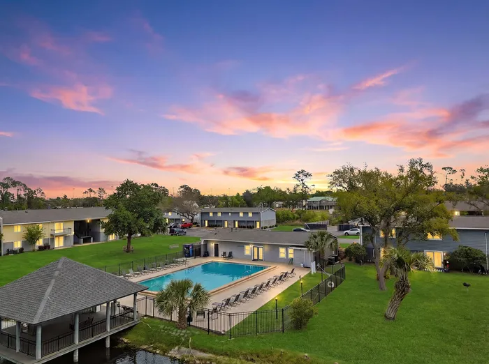 Charming residential community with a sparkling pool surrounded by lush greenery and a stunning sunset sky.