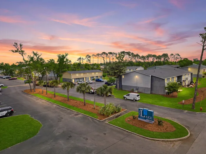 Charming apartment complex at sunset with lush landscaping, palm trees, and ample parking in a serene neighborhood.