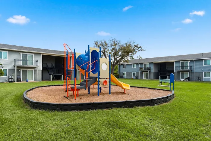 Bright apartment community with a vibrant playground set amid lush green lawns, perfect for family living and outdoor enjoyment.