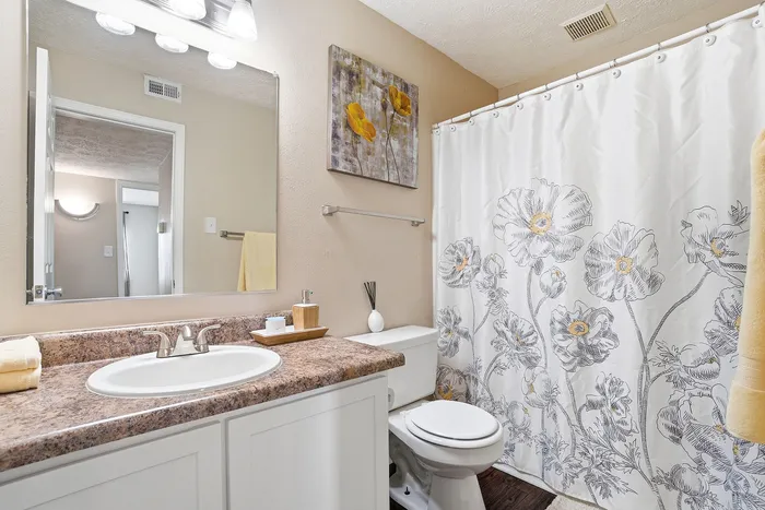 Bright and elegant bathroom featuring a floral shower curtain, granite countertop, and stylish decor accents.