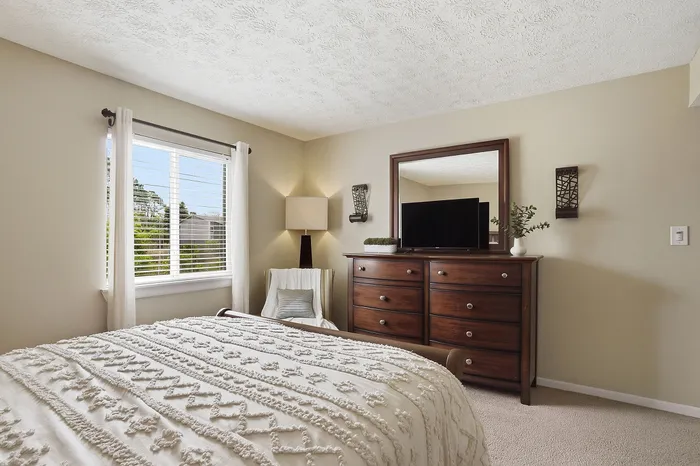 Bright and cozy bedroom with a large window, elegant drapery, and a stylish wooden dresser with a mirror.