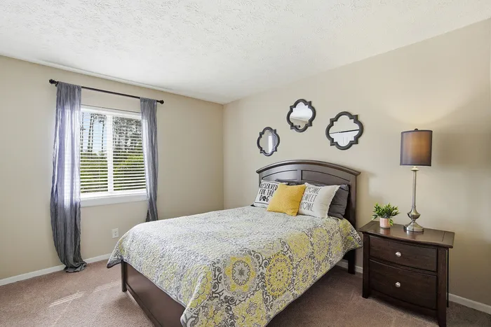 Cozy bedroom with a comfortable bed, decorative mirrors, and a stylish nightstand, bathed in natural light from a large window.