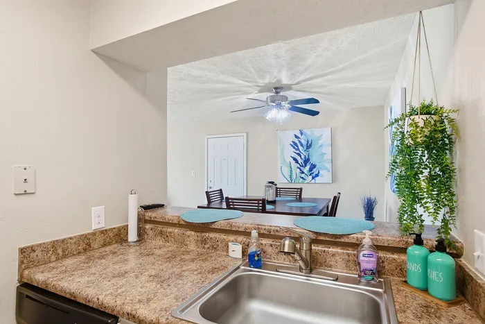 Inviting kitchen view with granite countertops, overlooking a chic dining area adorned with modern art and lush greenery.