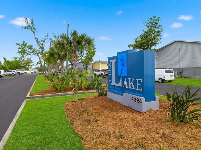 Inviting entrance sign for Turtle Lake Townhomes and Apartments surrounded by lush greenery and tidy landscaping.