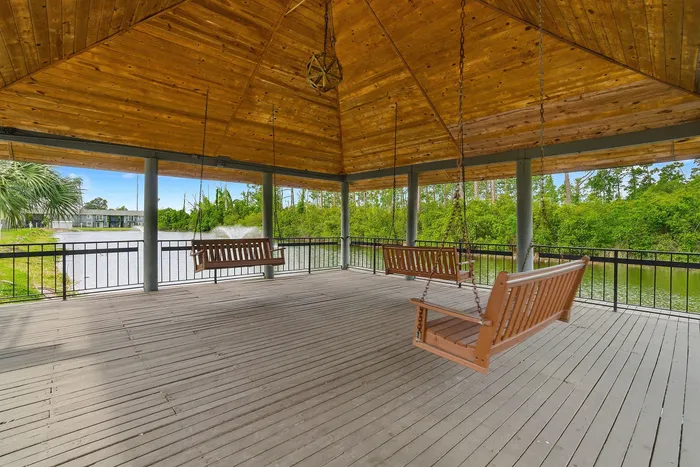 Charming wooden pavilion with elegant swings overlooking a tranquil pond and lush greenery, perfect for relaxation.