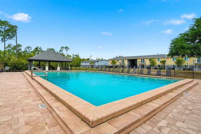 Inviting outdoor pool area with modern lounge chairs, surrounded by lush greenery and charming apartment views.