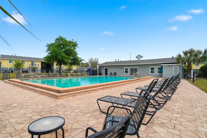 Inviting outdoor pool area with ample seating, surrounded by lush greenery and a clear blue sky, perfect for relaxation and leisure.